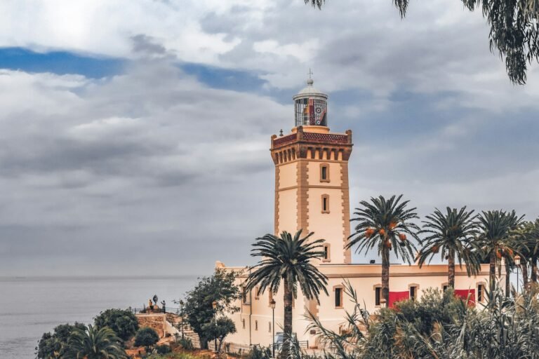 Tangier Travel lighthouse overlooking the Atlantic Ocean, surrounded by palm trees under a cloudy sky in Tangier, Morocco