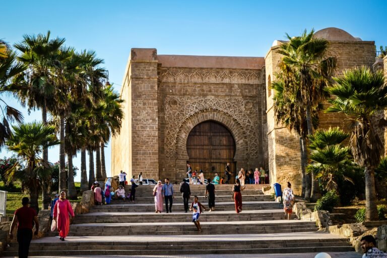 Rabat Travel scene showing visitors walking up the steps to the historic Chellah gate surrounded by palm trees in Rabat, Morocco